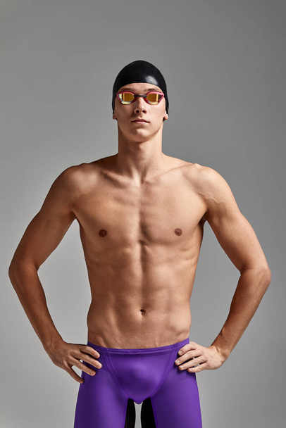 Portrait of a swimmer in a cap and mask, half-length portrait, young athlete swimmer wearing a cap and mask for swimming, copies of space, gray background - Photo, Image