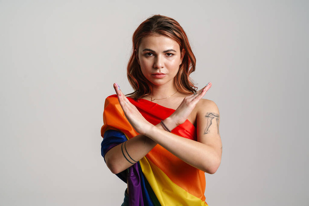 Serious woman wearing rainbow flag showing stop gesture isolated over gray background - Foto, immagini