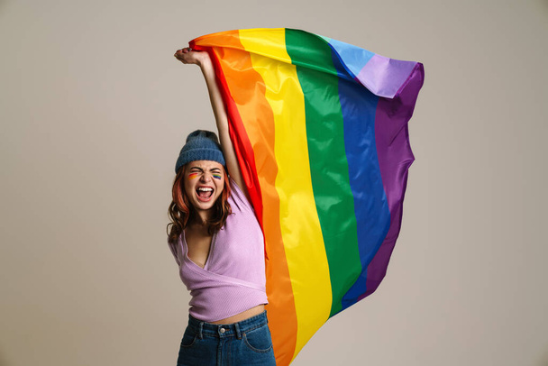 Excited beautiful woman screaming while with holding rainbow flag isolated over gray background - Foto, Imagen