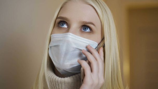 Close-up portrait of young girl in medical face mask is talking at phone. - Фото, зображення