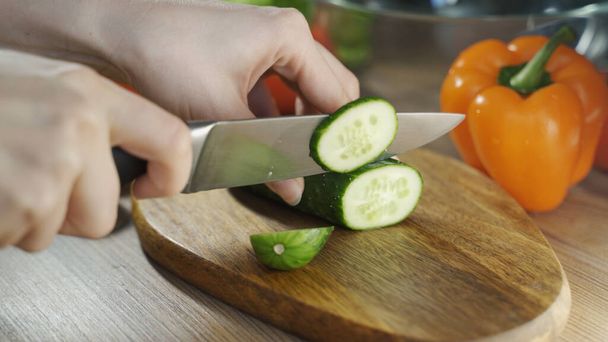 Preparation of salad. Cut vegetables on a wooden chopping Womens hands cut cucumber large, 4K video. - 写真・画像