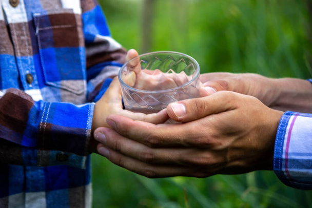 de l'eau dans un verre entre les mains d'un enfant et d'un père. La nature. Concentration sélective - Photo, image