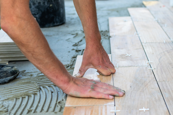 The hands of the professional tiler lying or installing modern, ceramic tile above cement on the garden terrace , tiling floor, building and pavement concept - Photo, Image