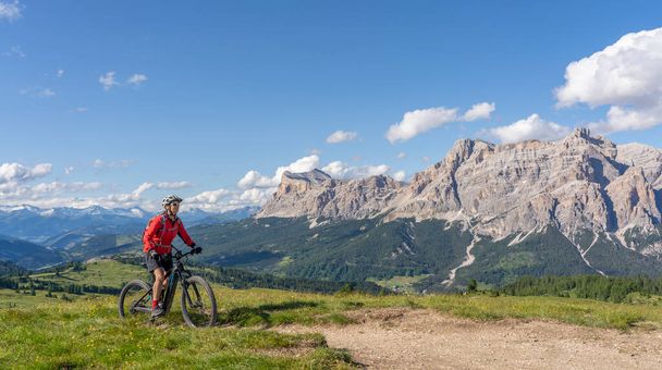 mulher sênior muito ativa montando sua bicicleta de montanha elétrica no planalto de Pralongia no Alta Badia Dolomites com incrível Sasso die Santa Cruce summit em Backg, Tirol do Sul e Trentino, Itália - Foto, Imagem