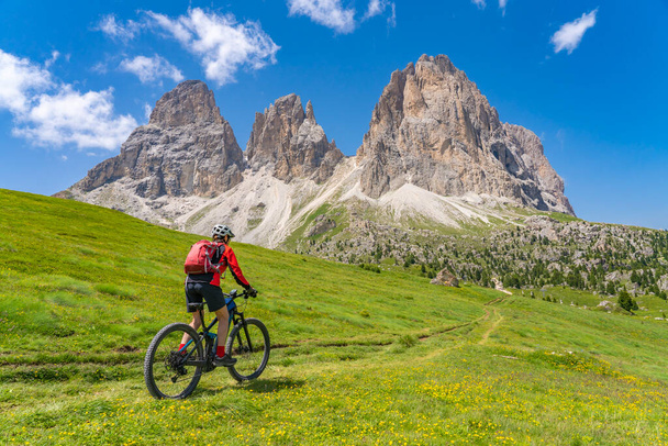 melko aktiivinen vanhempi nainen ratsastus hänen sähköinen maastopyörä alapuolella kuuluisa Sassolungo huippukokouksessa Sella Dolomites Selva Wolkenstein, Val Gardena, Etelä-Tirol ja Trentino, Italia - Valokuva, kuva