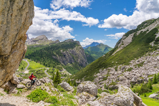 pretty active senior woman riding her electric mountain bike up to Valparola Pass  with awesome view down to Passo Falzarego in the Alta Badia Dolomites , South Tirol and Trentino, Italy - Foto, afbeelding