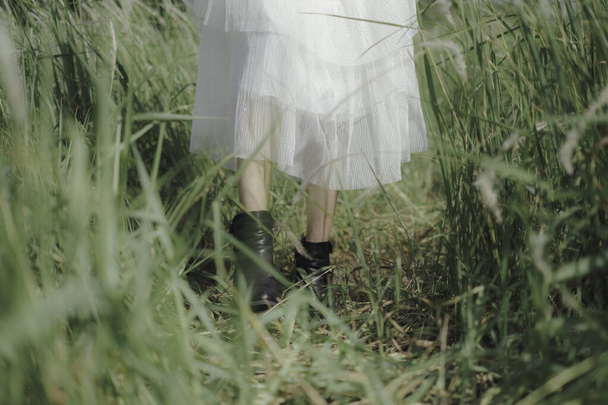 Großaufnahme einer Frau in weißem Kleid und schwarzem Stiefel, die auf der Wiese spaziert, der Sommer kommt, Freiheit, Konzept. - Foto, Bild