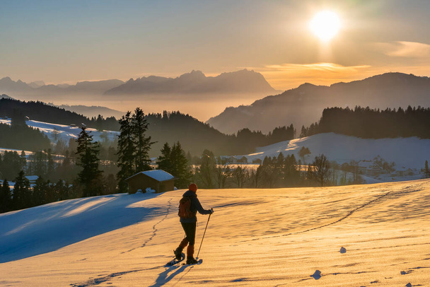 senior woman, snowshoeing in sunset in the Bregenzer Wald area of Vorarlberg, Austria with spectacular view on Mount Saentis, Switzerland - Zdjęcie, obraz