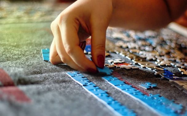 Mano de una mujer con esmalte de uñas jugando Jigsaw Puzzle, empezando a coincidir con las piezas para revelar la imagen. Trozos sobre fondo blanco. Juego de interior real bueno para el concepto de salud mental - Foto, Imagen