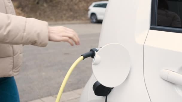 Nő jön az elektromos jármű és húzza ki tápegység kábel tölteni az utcán töltőponton  - Felvétel, videó