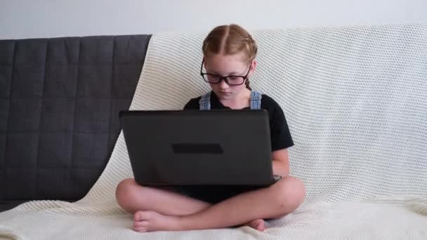  valkoihoinen punapää tyttö silmälaseissa kannettavan tietokoneen avulla opiskelee kotona - Materiaali, video
