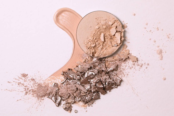 Crashed beige face finishing and liquid powder and crashed eyeshadow texture. Macro texture of make-up on beige background - Фото, зображення