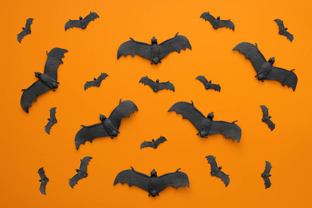 A lot of black bats flying on an orange background. Scary halloween flat lay composition on an orange background. Halloween decoration concept. - Fotó, kép