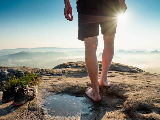 Hiker next to taken off shoes and water puddle on sandstone rock edge enjoy misty landscape view - Photo, Image