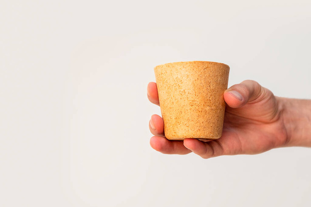 Male hand holding eco-friendly waffle coffee cup on neutral background with copy space - Photo, Image