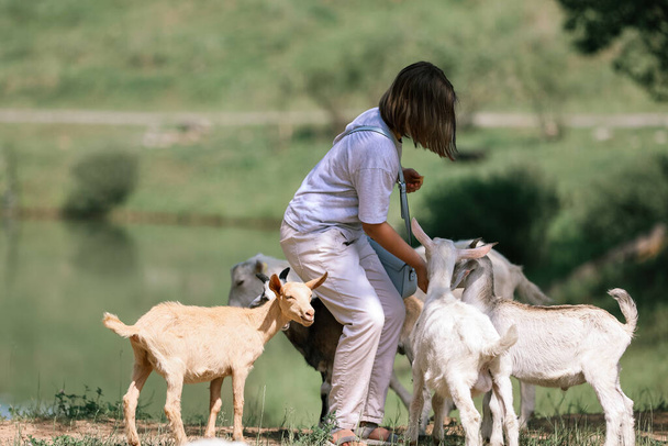 Chica alimenta y juega con cabras en una granja - Foto, imagen