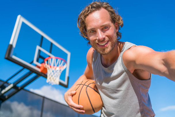 Basketball player man taking fun selfie photo at court net with basket ball. - Fotó, kép