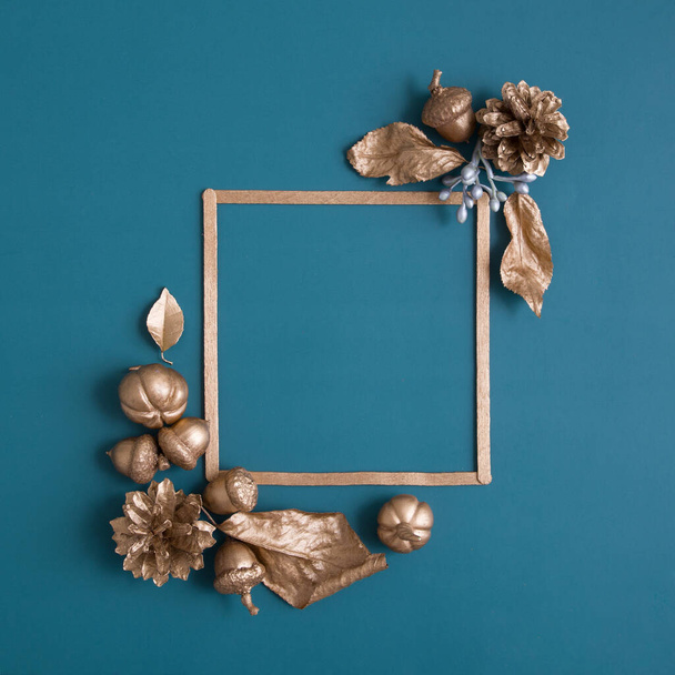 Still life of gold and white cones, pumpkins, acorns with a frame for text on a turquoise background. Minimalistic autumn concept with copy space - 写真・画像
