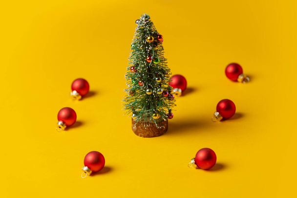 Little Christmas tree with baubles around on yellow background - Photo, image