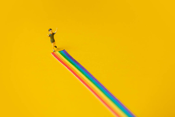 pequeño niño figura stand en arco iris LGBT tira sobre amarillo fondo - Foto, imagen