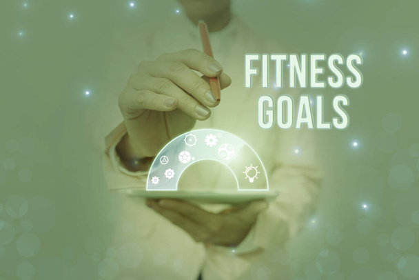 Text sign showing Fitness Goals. Internet Concept Loose fat Build muscle Getting stronger Conditioning Lady In Uniform Holding Pen Phone Showing Futuristic Virtual Interface. - Photo, Image