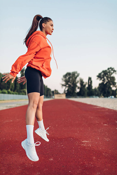 Young woman doing warm-up exercises on sportsground early in the morning - Photo, Image