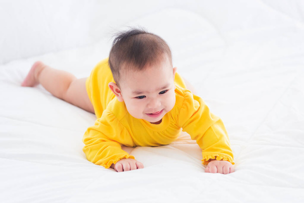 Portrait of beautiful young Asian newborn little baby prone on the bed at home, Happy baby smile wears a yellow shirt relaxing in the room, Family morning at home - Fotografie, Obrázek