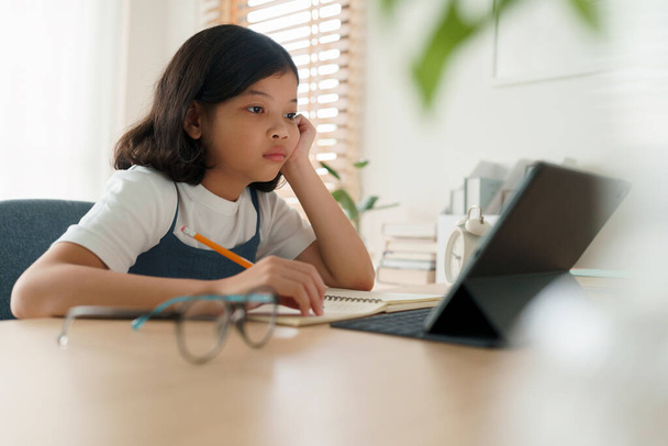 Asian little girl is sitting stressed and boring while studying online via internet with a tutor on tablet digital in morning, Concept online learning at home  - Фото, зображення