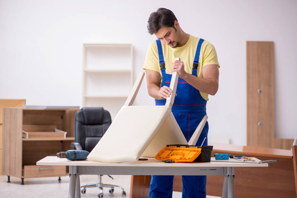 Молодой плотник-мужчина ремонтирует кресло в офисе - Фото, изображение