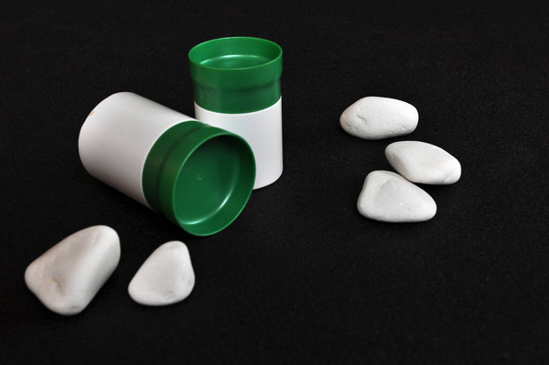 Dos recipientes médicos de plástico blanco para pastillas o vitaminas, para un estilo de vida saludable decorado con piedras blancas sobre fondo negro - Foto, Imagen