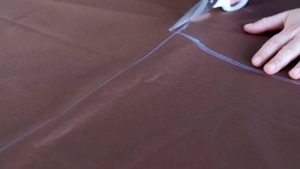 Vrouw handen met schaar snijden bruine stof volgens markeringen op tafelblad - Video