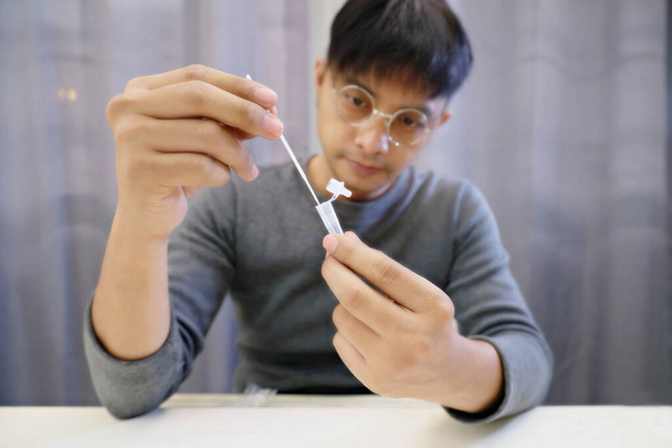 Man uses cotton wab to test for Covid-19 Włóż butelkę z odczynnikiem, aby poszukać czegoś, co jest uważane za wirus.Za pomocą narzędzia covid-19 self-tese (szybki test antygenu), wybierz ostrość. - Zdjęcie, obraz