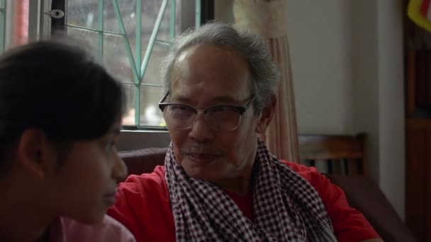 Gelukkig oudere Aziatische grootvader draagt een bril zittend en pratend met zijn schattige tienerkleindochter in de woonkamer. Verbindingsrelatie in familie van twee generaties. - Video