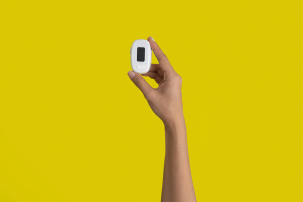Käsi pulssioksimetrillä tai veren happitason mittauslaitteella, jossa näyttö on eristetty keltaisella taustalla. Lääketieteen ja terveydenhuollon equipment.Coronavirus covid-19 puhkeaminen - Valokuva, kuva