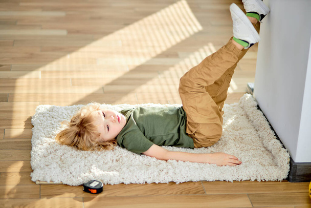 Child boy lying on carpet floor at home, relaxing, having rest alone, side view - Fotoğraf, Görsel