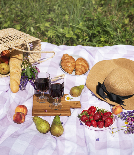 Romantische picknick scene op zomerdag. Outdoor picknick met wijn en een vrucht in de open lucht op de achtergrond van groen gras. - Foto, afbeelding