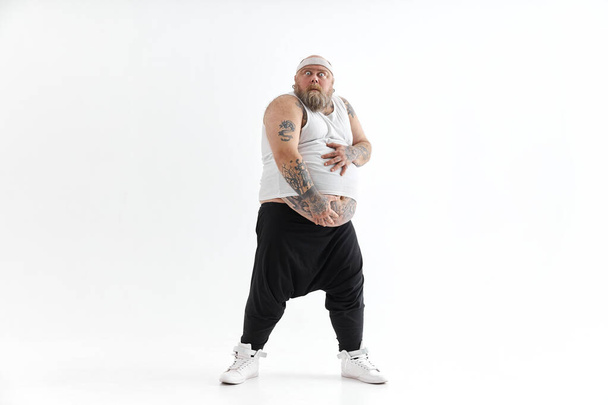 Heureux homme gras avec gros ventre et tatouages dans les vêtements de sport tient son estomac - Photo, image
