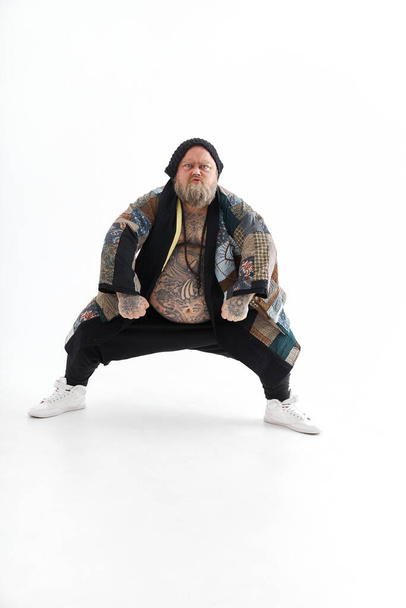 Fat stylish bearded tattoed caucasian man with big belly is posing and dancing wearing ethnic kimono - Foto, afbeelding