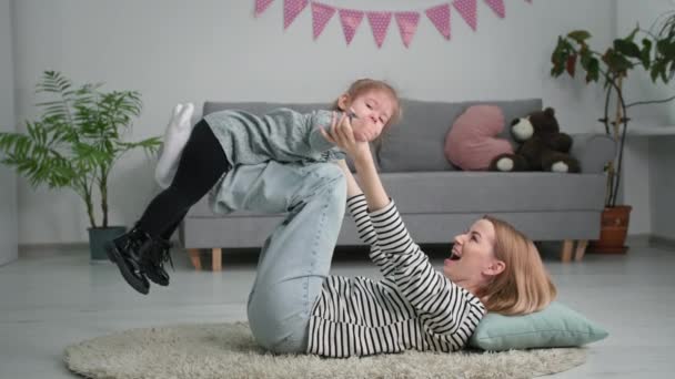 dzieciństwo, mała radosna dziewczynka bawiąca się ze swoją szczęśliwą matką w samolocie leżącą na podłodze w salonie - Materiał filmowy, wideo