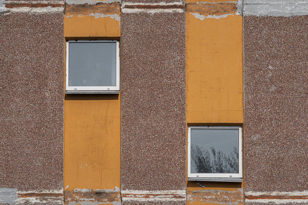 İki dekoratif penceresi ve dikey turuncu çizgileri olan eski püskü beton bir evin ayrıntıları. Yakın plan, desenli.. - Fotoğraf, Görsel