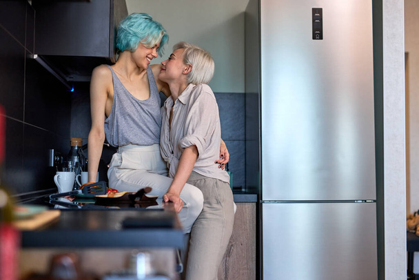 Pretty Same Sex Young Female Couple Hugging Kissing In Kitchen At Home Together - 写真・画像