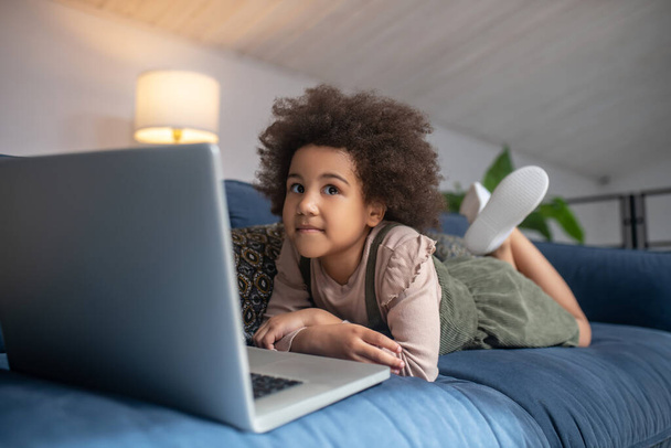 Little girl lying on couch near laptop - Photo, image
