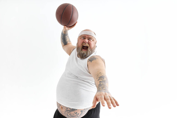 bearded fat caucasian tattoed man with basketball ball in white background. He is funny and happy - Fotoğraf, Görsel