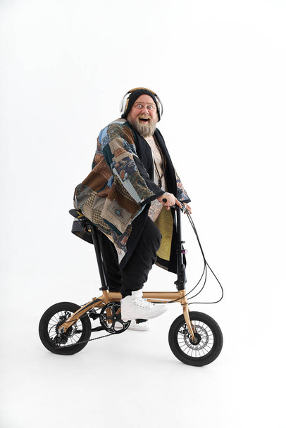 Big fat tattoed caucasian man in kimono is holding little bicycle and smilling - Фото, зображення