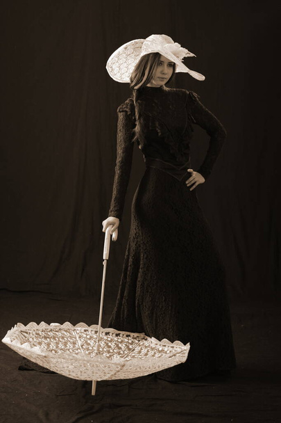 A girl in an old dress and hat stands on a dark background and is sad - Foto, Bild