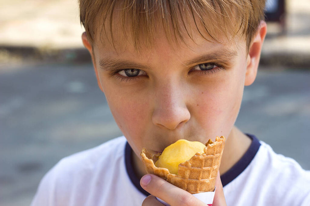 Portret van een kind jongen close-up met plezier eten van ijs in een wafelbeker - Foto, afbeelding