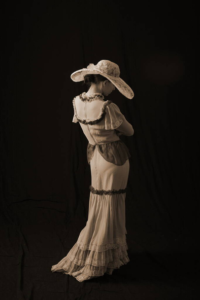 A girl in an old dress and hat stands on a dark background and is sad - Foto, immagini