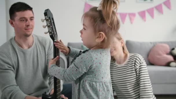 niñez, pequeña linda chica sonriente con guitarra se divierte con sus padres en la sala de estar durante el ocio familiar - Metraje, vídeo