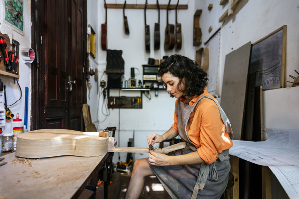 mujer luthier haciendo guitarras en su taller de instrumentos musicales - Foto, Imagen
