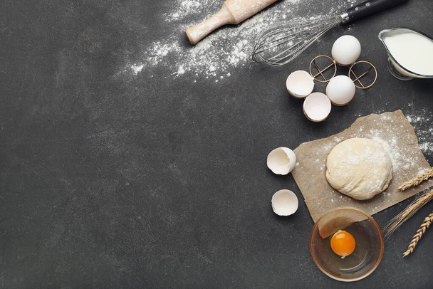 Свежее тесто с ингредиентами для приготовления хлебобулочных изделий и посуды на тёмном фоне - Фото, изображение